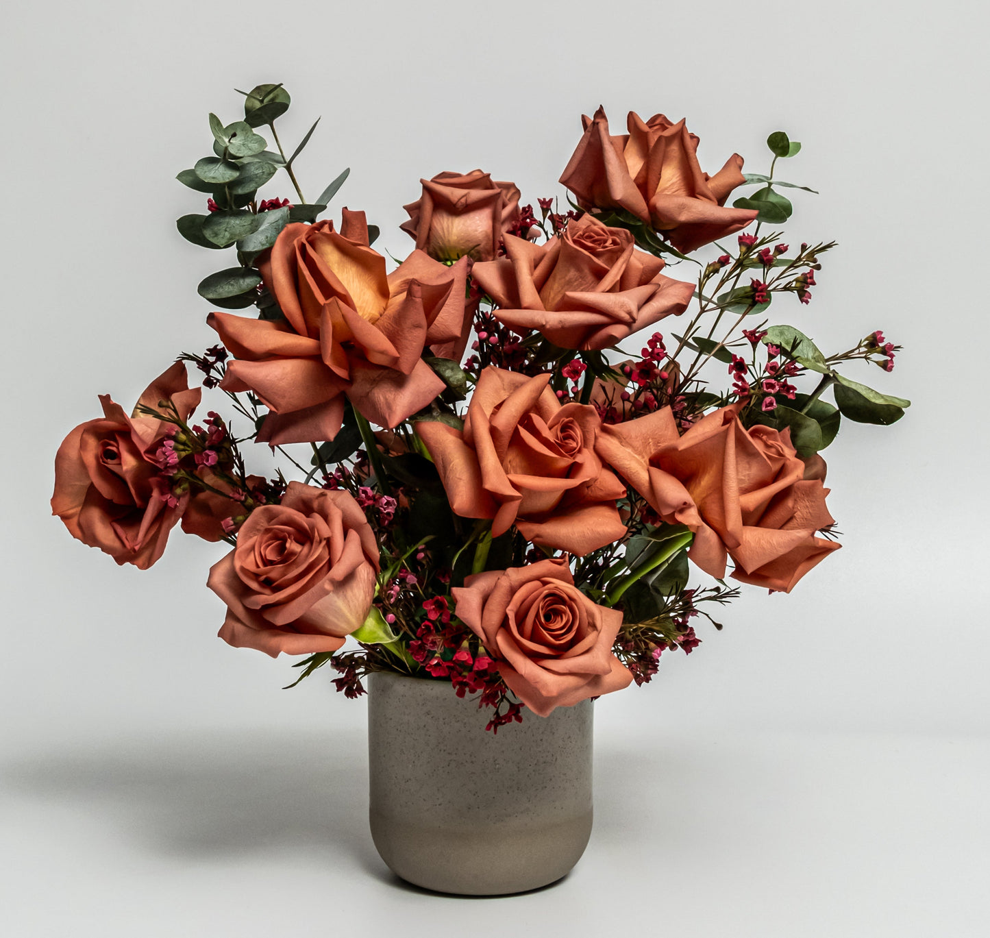 Terracotta rose and red accent flower arrangement with eucalyptus in a matte stone vase – handcrafted modern design by Rainbow Floral Toronto.