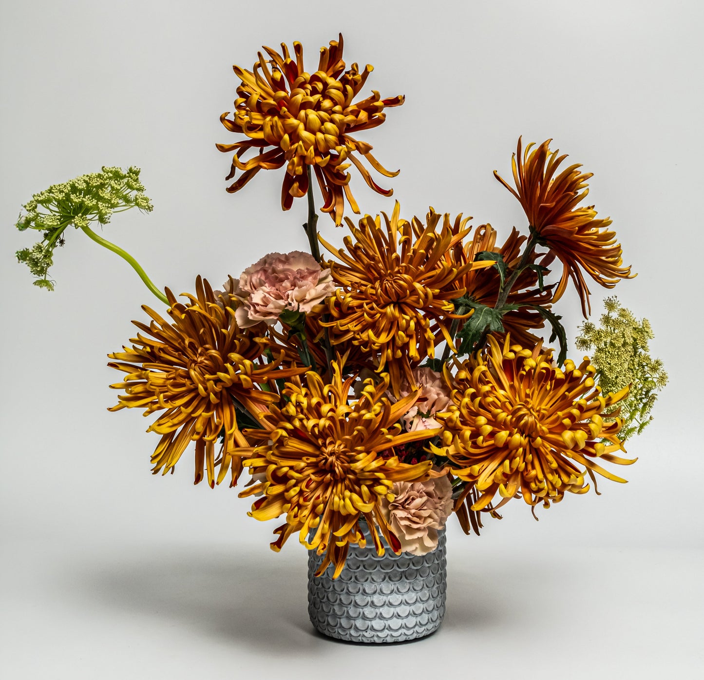 Golden chrysanthemum and blush carnation arrangement in a textured grey vase – handcrafted autumn floral design by Rainbow Floral Toronto.