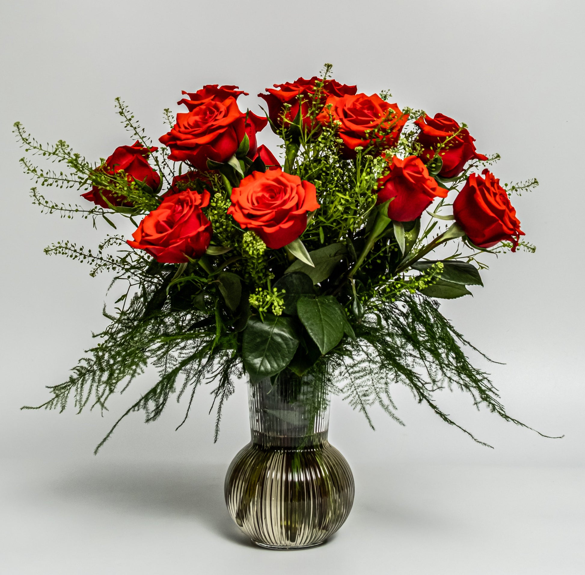 Classic red rose vase arrangement with lush greenery in a smoked glass vase – handcrafted romantic floral design by Rainbow Floral Toronto.
