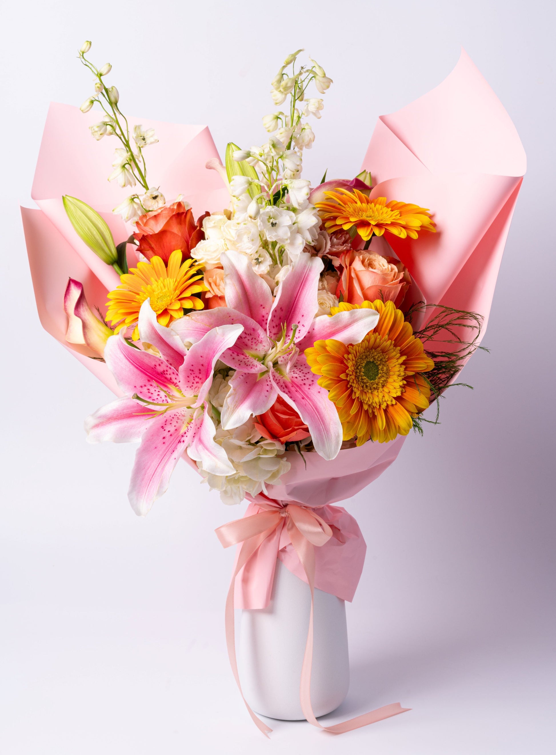 Bright wrapped bouquet with lilies, gerbera daisies, roses, and delphinium. A cheerful and vibrant gift. Toronto same-day flower delivery