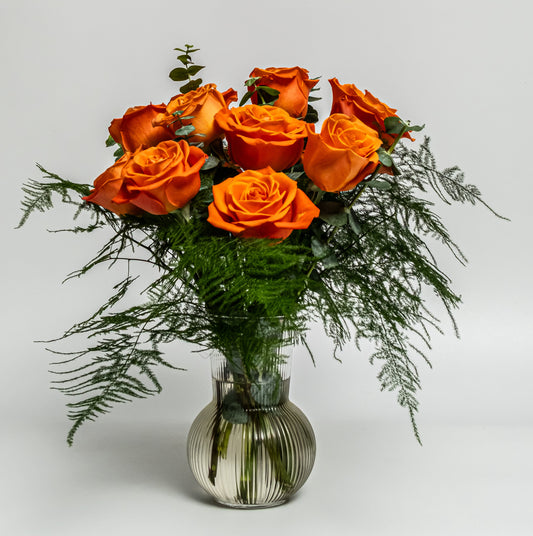 Vibrant orange rose arrangement with greenery in a ribbed smoked-glass vase – handcrafted bold floral design by Rainbow Floral Toronto.